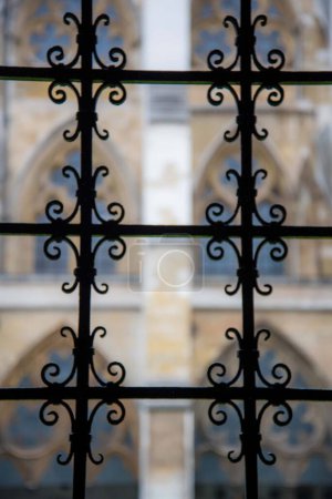 Photo for "Artistic view of gothic iron gate juxtaposed with cathedral windows blurred in background. Unique perspective" - Royalty Free Image