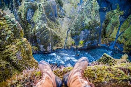 Foto de "Islandia cañón verde musgoso con impresionantes vistas. Vista de los pies de los excursionistas con botas con vistas al río que fluye a través del cañón." - Imagen libre de derechos