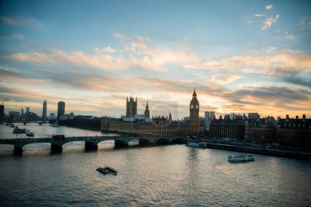 Foto de "Vista del horizonte de Londres al atardecer con monumentos famosos, Big Ben, Casas del Parlamento y barcos en el río Támesis con hermoso cielo azul y amarillo." - Imagen libre de derechos
