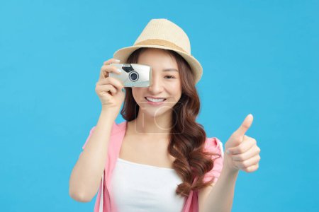 Téléchargez les photos : Portrait d'une jolie fille souriante en robe prenant des photos sur un appareil photo isolé sur fond bleu - en image libre de droit