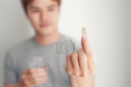 Foto de Hombre guapo sonriente borroso sosteniendo la píldora de gel suave omega 3 en sus dedos - Imagen libre de derechos