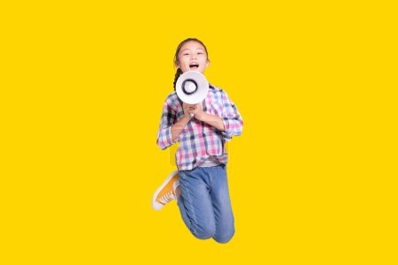 Téléchargez les photos : Fille sautant avec mégaphone.Isolé sur fond jaune. - en image libre de droit