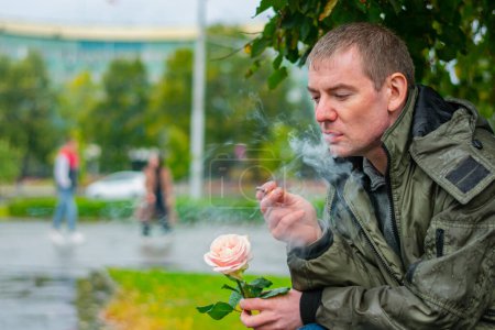 Photo for Smoking man with a rose sits in the park thinking - Royalty Free Image