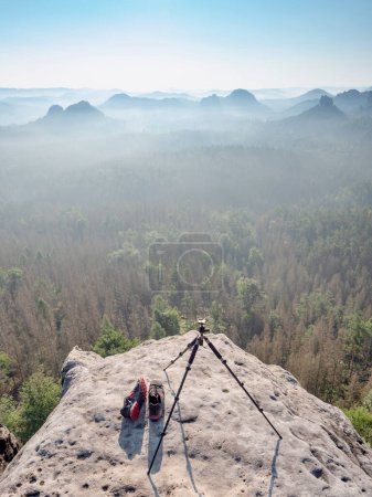 Téléchargez les photos : Caméra moderne trépied léger sur point de vue rocheux fin de matinée brumeuse - en image libre de droit
