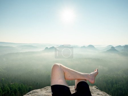 Foto de Ver arriba cuerpo masculino descalzo en pantalones negros durmiendo en el acantilado - Imagen libre de derechos