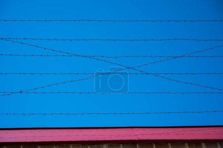 Foto de Alambre de púas en la cerca de la prisión contra el cielo azul" - Imagen libre de derechos
