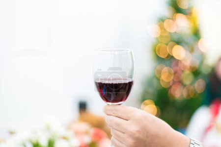 Téléchargez les photos : Verre de vin rouge pour trinquer à la fête avec fond d'arbre de Noël. Concept de célébration et d'anniversaire. Nouvel an toast et concept de boisson - en image libre de droit