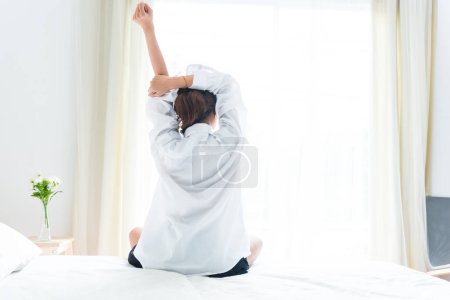 Photo for Back view of woman stretching in morning after waking up on bed near window. Holiday and Relax concept. Lazy day and Working day concept. Office woman and worker in daily life theme - Royalty Free Image