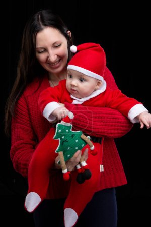Foto de Mamá y su hijito en Navidad. Una mujer sostiene a su hijo en sus brazos, que está vestido con ropa de Santa Claus. - Imagen libre de derechos
