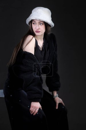 Téléchargez les photos : Belle fille élégante dans un chapeau de fourrure sur un fond sombre. - en image libre de droit