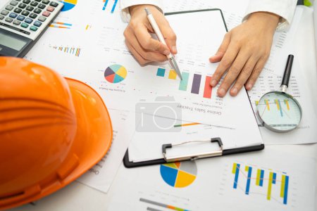 Photo for Engineer working project accounting with graph and construction helmet in office, Construction account concept. - Royalty Free Image