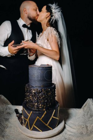 Foto de Elegante novia y novio beso con un pastel en sus manos en la noche en la boda - Imagen libre de derechos