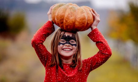 Photo for "Smiling little girl holding pumpkin above head" - Royalty Free Image