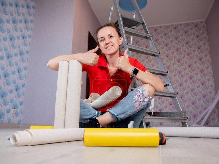 Photo for "A woman is sitting on the floor in a room with rolls of Wallpaper. Concept of renovation in the apartment." - Royalty Free Image
