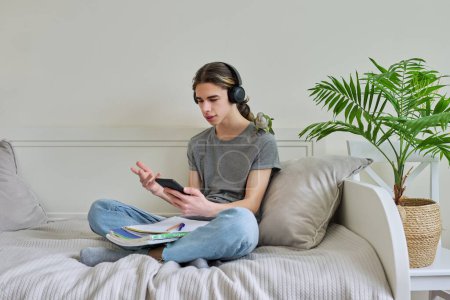 Photo for "Male teenager in headphones with smartphone using video call, parrot on shoulder" - Royalty Free Image