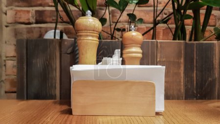 Foto de "Una mesa en un café o restaurante. Servilletas blancas en un soporte de madera, sal y pimienta en una mesa de madera. Soporte de pizza con especias, servilletas y palillos de dientes" - Imagen libre de derechos