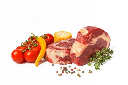Photo for "two fresh marbled beef steaks on a white plate with vegetables cherry tomatoes on a sprig, corn, spicy yellow pepper, a sprig of rosemary, salt and different varieties of peppers" - Royalty Free Image