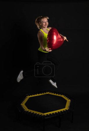Téléchargez les photos : Fille sur un trampoline de remise en forme sur un fond noir dans un t-shirt jaune sport d'énergie jaune, mouvement d'athlète d'activité active fille, club. Mouvement de mouche, instructeur de muscle de vêtements de sport profiter - en image libre de droit