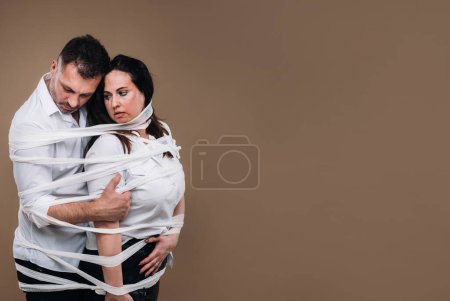 Foto de "Un hombre agresivo abraza a una mujer maltratada y se envuelve en vendajes juntos. Violencia doméstica" - Imagen libre de derechos
