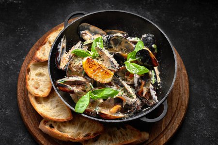 Photo for Cooked mussels in a skillet with cheese and basil leaves, on a wooden board - Royalty Free Image