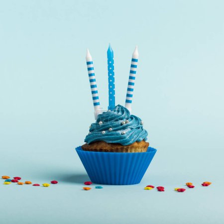 Téléchargez les photos : Muffin décoratif avec bougies et aspersions étoiles sur fond bleu - en image libre de droit