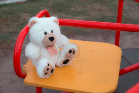 Téléchargez les photos : Gros plan Un ours en peluche est assis sur une balançoire pour enfants en rouge. Le concept de tristesse, perte, mort, deuil, orphelinat ou solitude - en image libre de droit