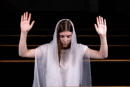 Foto de Una joven modesta con un pañuelo en la cabeza está sentada en la iglesia y rezando. El concepto de religión, oración, adoración - Imagen libre de derechos