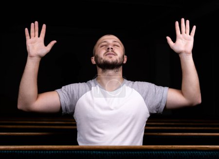 Foto de Un hombre cristiano con camisa blanca está sentado con las manos en alto y rezando con humilde corazón en la iglesia - Imagen libre de derechos