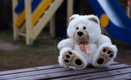 Photo for Sad lonely teddy bear. White fluffy teddy bear lonely sits on an old wooden bench in a overgrown garden - Royalty Free Image