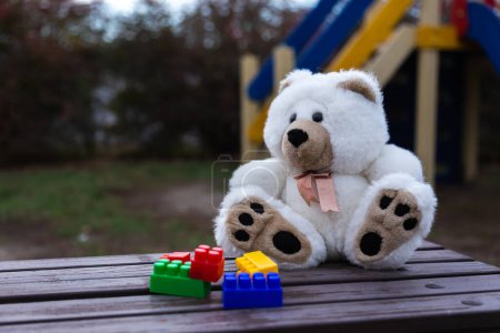 Téléchargez les photos : "Sad lonely teddy bear. White fluffy teddy bear lonely sits on an old wooden bench in a overgrown garden" - en image libre de droit