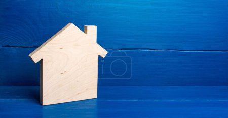 Plan en bois en forme de figurine de maison sur un fond bleu. Minimalisme. Concept immobilier. Acheter et vendre. Logement, services immobiliers. Industrie de la construction, entretien des bâtiments. Prêt hypothécaire