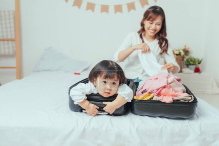 Photo for "mother prepares clothes to put in her suitcase and her daughter plays with her suitcase" - Royalty Free Image