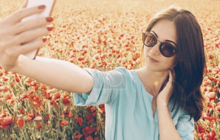 Foto de Mujer bonita tomando selfie en campo de flores de amapola - Imagen libre de derechos