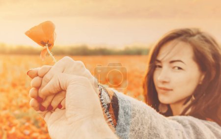 Foto de "Mujer sosteniendo mano masculina con flor de amapola." - Imagen libre de derechos