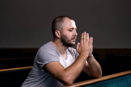 Téléchargez les photos : "Un chrétien en chemise blanche est assis et prie avec un cœur humble dans l'église
" - en image libre de droit