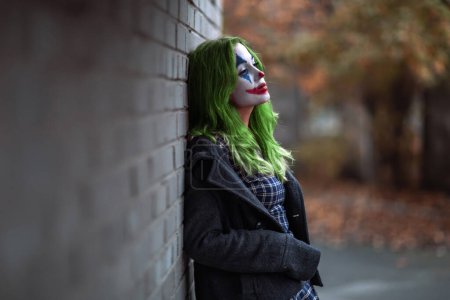 Foto de "Retrato de una chica de pelo verde en vestido de chekered con maquillaje joker sobre un fondo de pared de ladrillo
." - Imagen libre de derechos