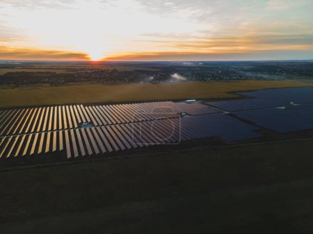 Téléchargez les photos : "Vue aérienne sur drone dans de grands panneaux solaires dans une ferme solaire dans un grand champ sur la campagne au coucher du soleil lumineux. Centrales solaires à cellules." - en image libre de droit