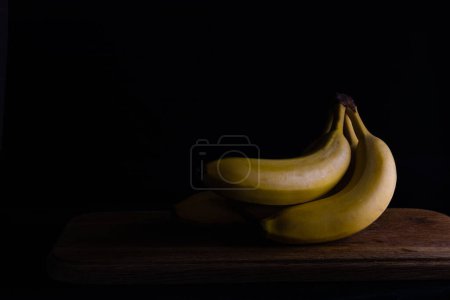 Téléchargez les photos : "bananes sur une planche de bois sur un fond sombre" - en image libre de droit