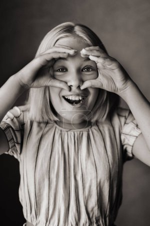 Téléchargez les photos : "Un enfant heureux, une petite fille en T-shirt gris sur fond beige.Photo noir et blanc" - en image libre de droit