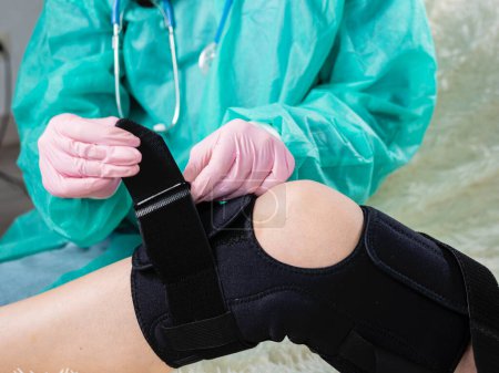 Téléchargez les photos : "Gros plan d'une physiothérapeute qui applique une attelle sur l'articulation du genou. Lésion aux jambes" - en image libre de droit