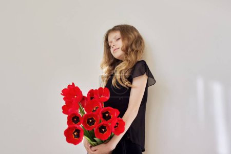Téléchargez les photos : Triste enfant fille avec un bouquet de tulipes rouges en robe noire - en image libre de droit