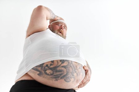 Foto de Hombre gordo con gran vientre y tatuajes en ropa deportiva está sosteniendo su estómago con emoción conmocionada - Imagen libre de derechos