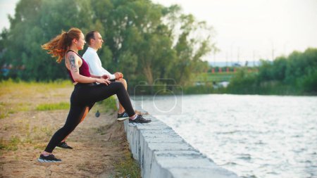 Photo for Man and woman stretching leg muscles resting their feet standing near the waterfront - Royalty Free Image