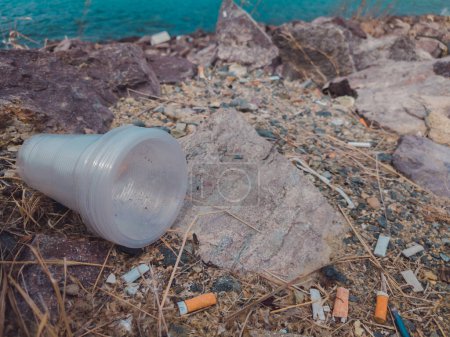 Foto de Mucha basura esparcida por el suelo, residuos cerca del mar en la playa. Problema del medio ambiente desastre y contaminación. Ecología del planeta. Volcado no autorizado de basura al aire libre - Imagen libre de derechos