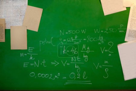 Foto de Fórmulas matemáticas y papeles en una pizarra verde - pizarra y concepto escolar - Imagen libre de derechos