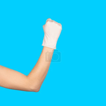 Photo for Hand in a white latex glove showing Solid fist or anger gesture isolated blue, background. - Royalty Free Image