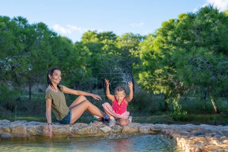 Photo for Beautiful mother and her little daughter outdoors. Beauty Mum and her Child playing with water in Park together at sunset. Outdoor Portrait of happy family. Mother's Day - Royalty Free Image