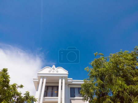 Téléchargez les photos : Le toit de la maison avec une belle fenêtre sous le ciel bleu et des arbres vert vif. Vente et location de concept immobilier - en image libre de droit