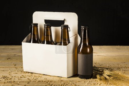 Photo for Beer bottle carton box and ears of wheat on wooden surface - Royalty Free Image