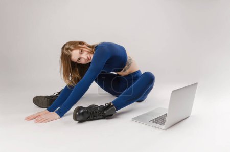 Photo for Athletic girl posing in the Studio performing exercises online on a laptop on a white background - Royalty Free Image